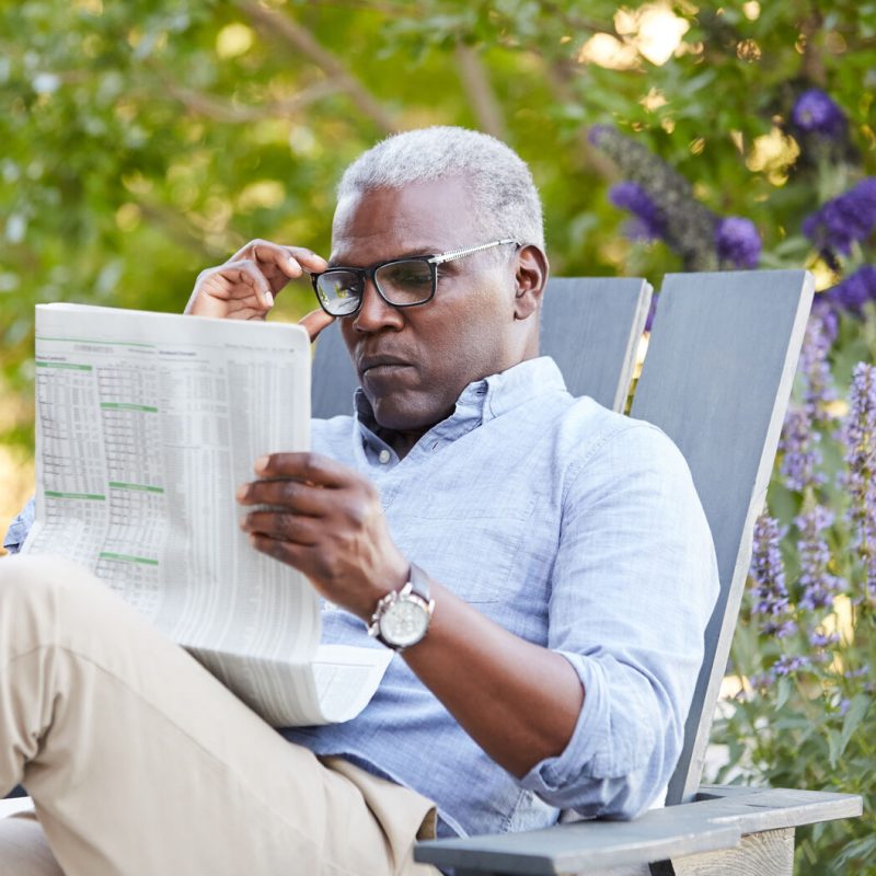 Portrait Of African American Senior Man Reading The Newspaper On His Patio Outside