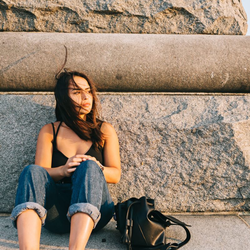 Pensive Teen Sitting On Stone Monument Alone